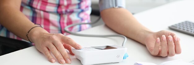 Woman sitting at table measures blood pressure with automatic tonometer