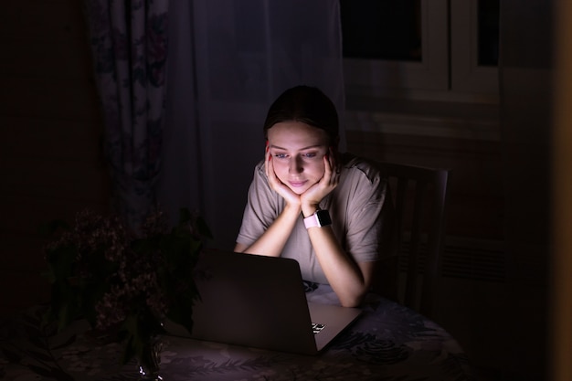 Woman sitting on the table, watching a movie on laptop late at night, can not sleep, sharing social media