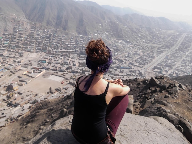 Woman sitting on top of a hill looking at a city in the distance