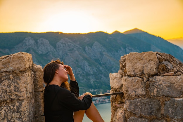 Photo woman sitting on top of hill on sunset with beautiful view of kotor