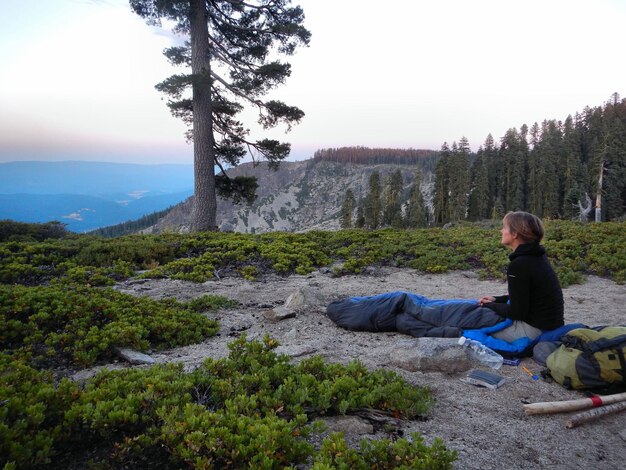 Photo woman sitting on tree looking at mountain against sky