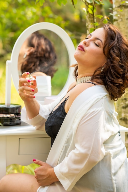 Foto donna che si siede e che utilizza profumo nella foresta