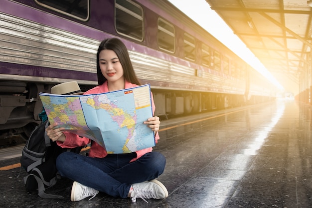 女性、座って、夏の列車駅で地図を表示