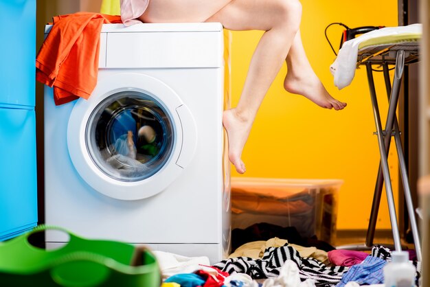 Woman sitting on the washing machine at the loundry. Close-up view on the machine and legs