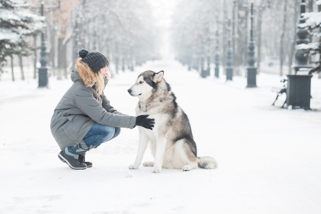 Woman sitting with alaskan malamute in winter city. . 