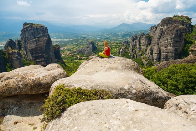 Woman sitting with back to camera observing great scenic and  meditative view from the top of a rock in Meteora, Greece