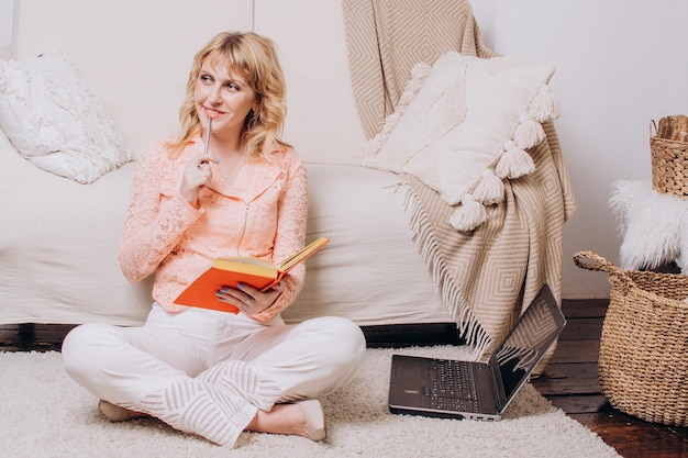 Woman sitting with book and laptop on the floor