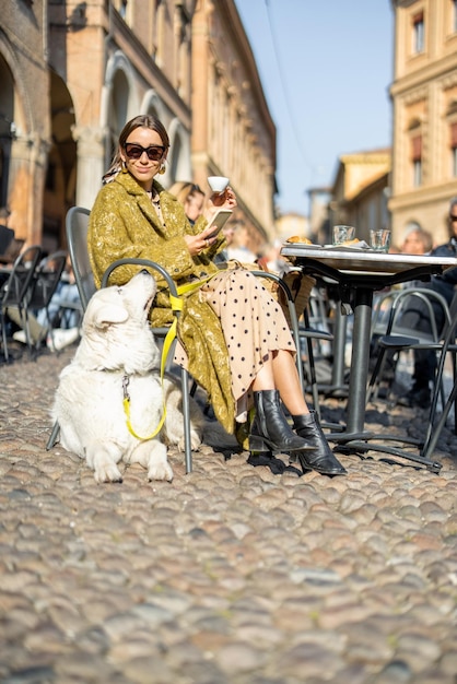 Woman sitting with her white dog at outdoor cafe in the old town of bologna city