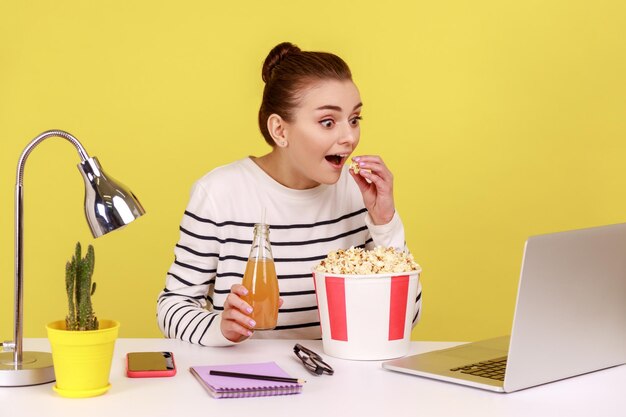 Woman sitting at workplace watching movie during resting looking at laptop screen with open mouth