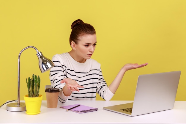Woman sitting at workplace with laptop and looking at laptop screen with angry indignant expression