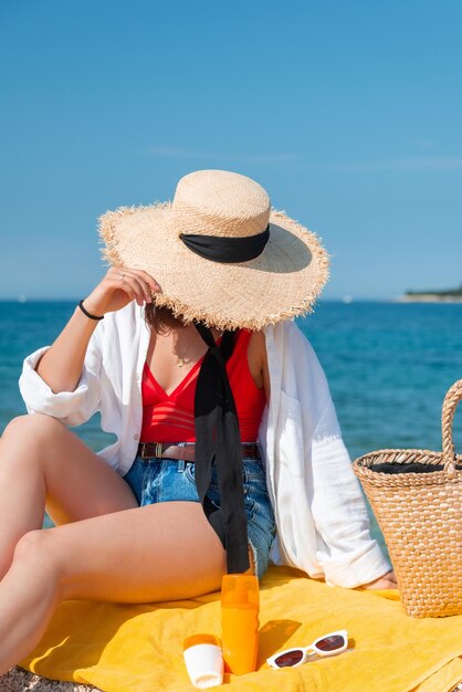 여름 옷을 입고 바다 해변에서 노란 담요에 앉아 있는 여자