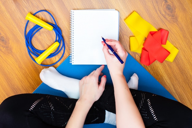 Woman sitting on yoga mat writting with a pen in an empty notebook.