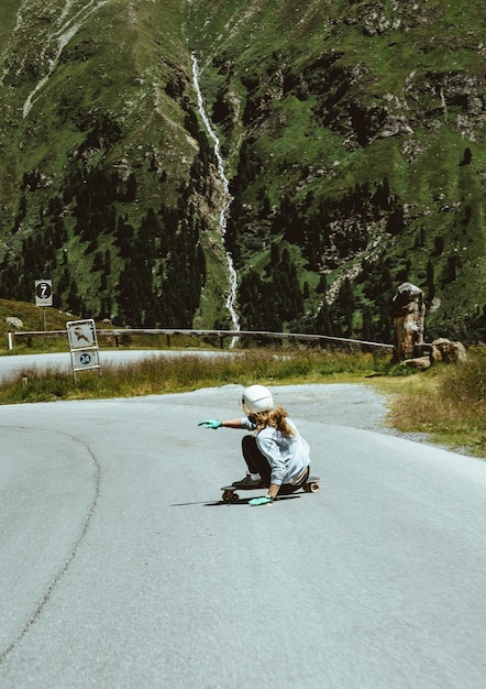 Женщина катается на скейтборде и делает трюки между поворотами на горном перевале