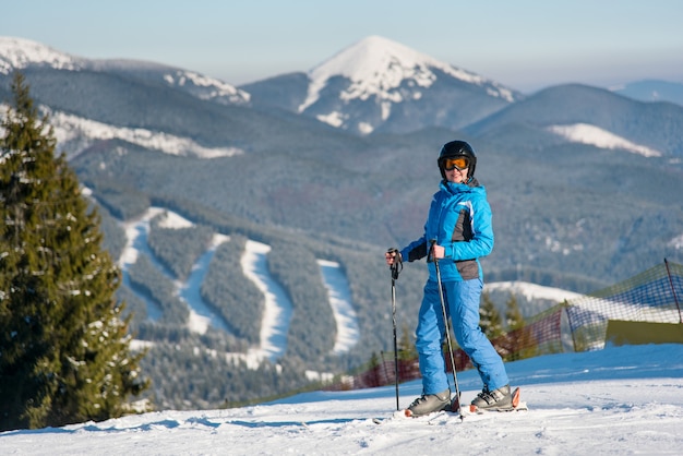 冬のスキーリゾートで山でスキーをしながら楽しくカメラに笑顔の女性スキーヤー