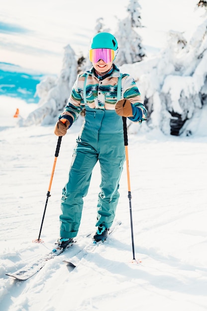 Woman in skiing clothes with helmet and ski googles on her head with ski sticks Winter weather on the slopes On top of a mountain and enjoying view Alpine skier Winter sport