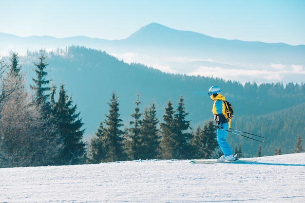 Woman skiing down by winter slope mountains on background