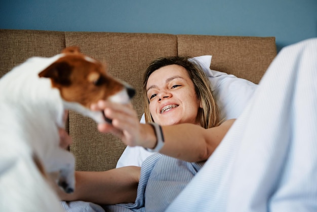 ベッドで寝て犬と遊ぶ女性