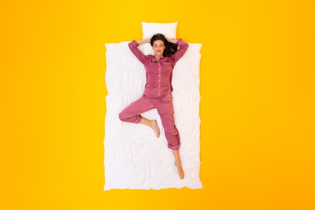 Woman sleeping holding hands behind head lying over yellow background