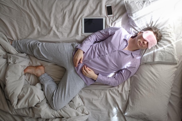 Woman in sleeping mask having a nap on the bed being tired of working home