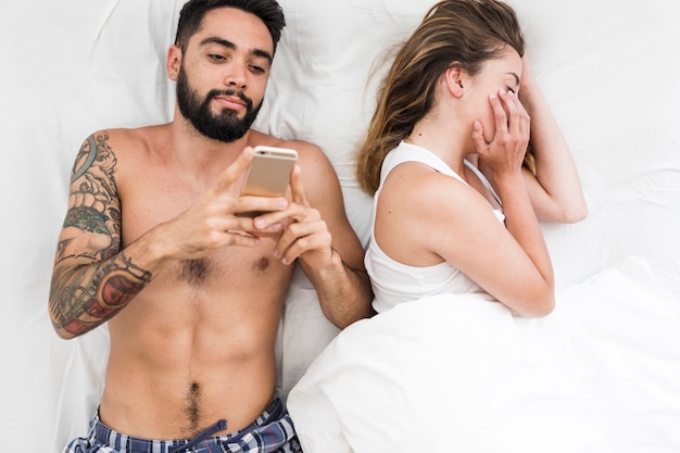 Woman sleeping near her husband using mobile phone