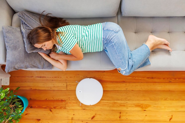 Foto una donna che dorme sul divano mentre l'aspirapolvere robot si occupa tranquillamente della pulizia