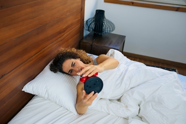 Woman sleeping and wake up to turn off the alarm clock in the morning.