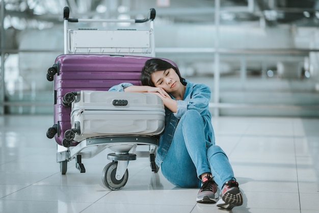 woman sleeping with luggage trolley at airport 