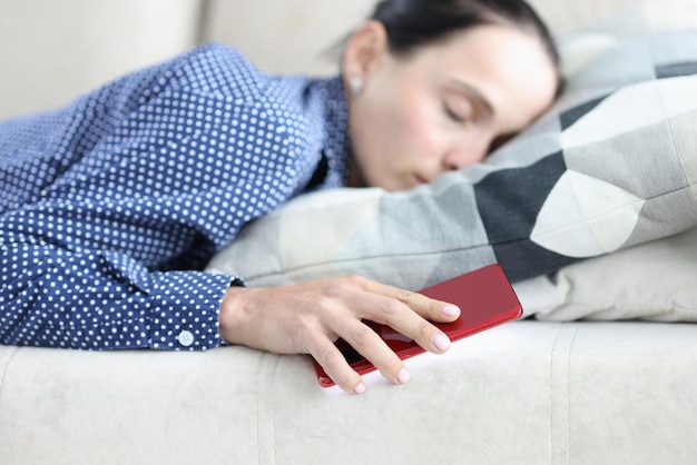 Woman sleeps on sofa and holds smartphone call waiting and\
message concept