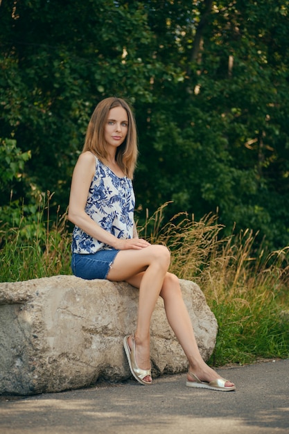 Woman in sleveless blouse and denim skirt having rest at country recreation area, enjoying fresh air and calmness