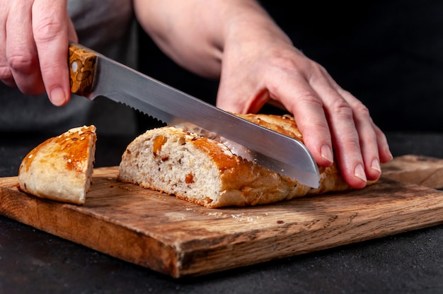 Woman Slices Homemade Wholemeal Multigrain Bread with Flax Seeds and Sesame on Wooden Board on Dark Table