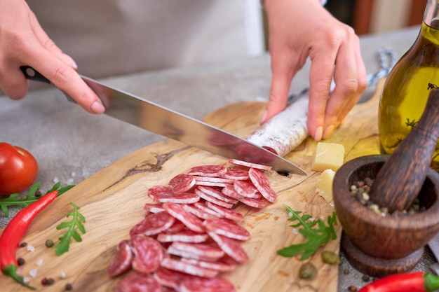 Photo woman slicing spanish sausage fuet salami with knife on a domestic kitchen