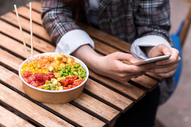 A woman in smartphone and poke bowl in a park