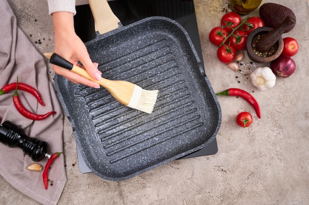 Woman smear olive oil on grill frying pan with silicone brush at domestic kitchen