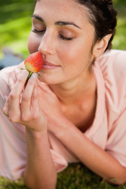 Photo woman smells an strawberry while lying in grass