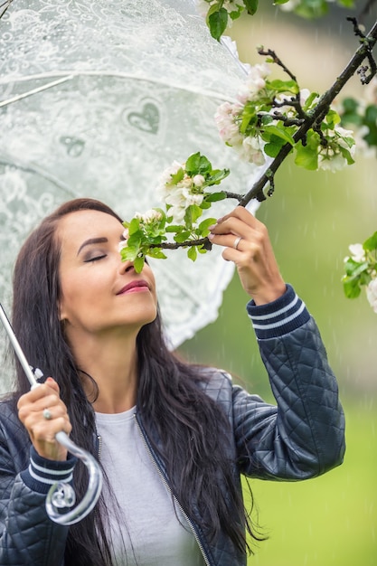여자는 우산을 들고 자연 속에서 봄 비오는 날 나무 꽃 냄새를 맡습니다.