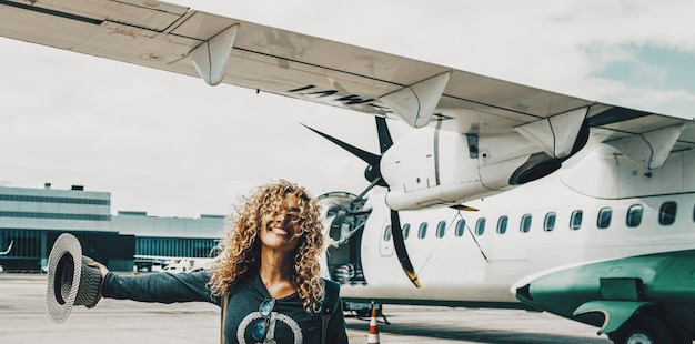 Woman smile and celebrate the arrival at her summer holiday travel vacation destination Happy female people portrait with airplane flight in background inside the airport Wanderlust lifestyle