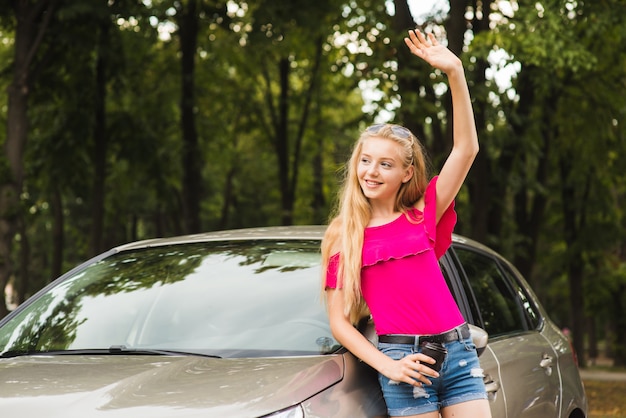 Женщина улыбается и приветствует рукой возле машины