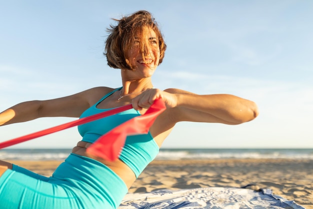 A woman smiles happily while doing Pilates exercises on the beach