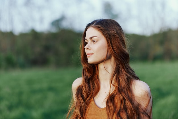 A woman smiles and is happy in nature in a green park looks at the sunset and smiles Healthy lifestyle concept High quality photo