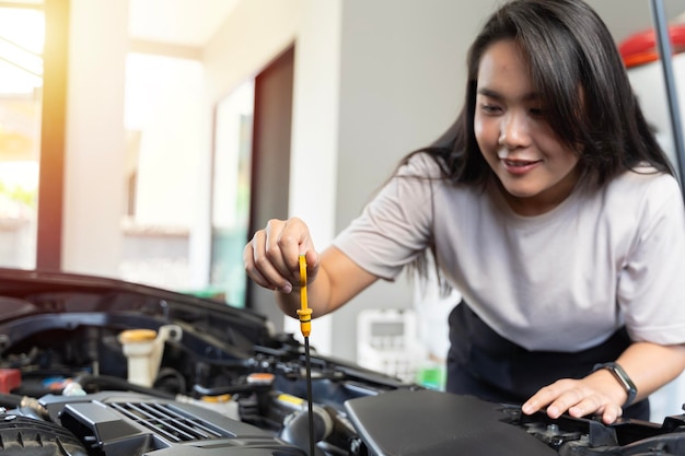 Женщина улыбается, проверяя масло в двигателе машины Женщина проверяет масло в двигатели машины в тени, работая