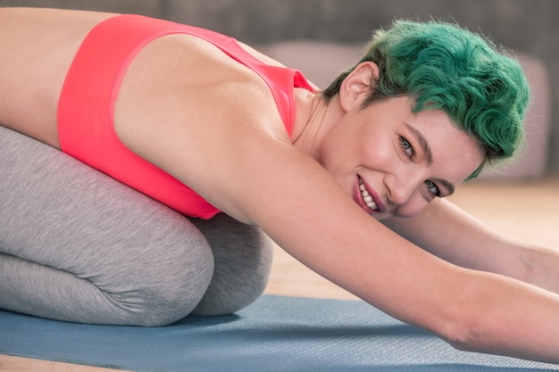 Woman smiling. Appealing mature green-eyed woman smiling while stretching after gym in the morning