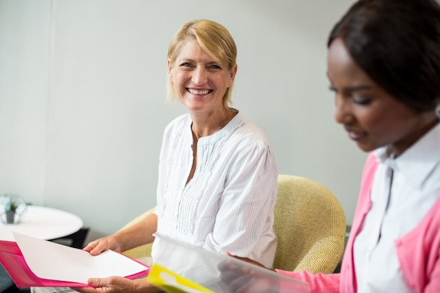 Photo woman smiling at camera while her colleague reading document