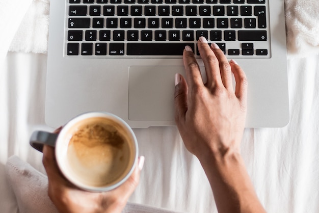 Donna che sorride bevendo un caffè e lavorando con il suo computer sul letto