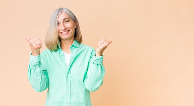 woman smiling joyfully and looking happy, feeling carefree and positive with both thumbs up