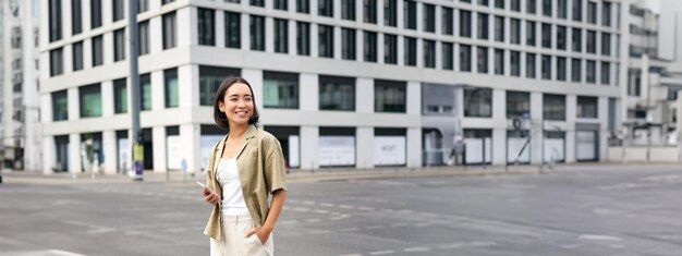 Photo woman smiling standing with smartphone on street waiting for taxi checking mobile phone app