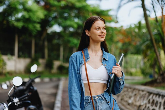 Woman smiling walking in the park outside with laptop freelancer against a backdrop of green palm trees in summer tropical backdrop blogger on a trip work online