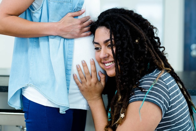 woman smiling while listening to pregnant partners stomach