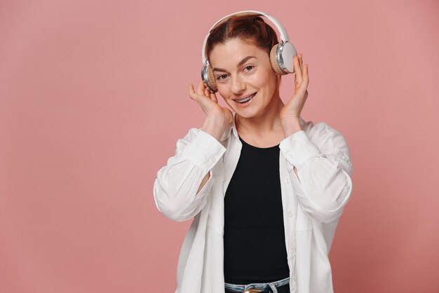 Woman smiling with braces on her teeth and listening to music in headphones on pink background