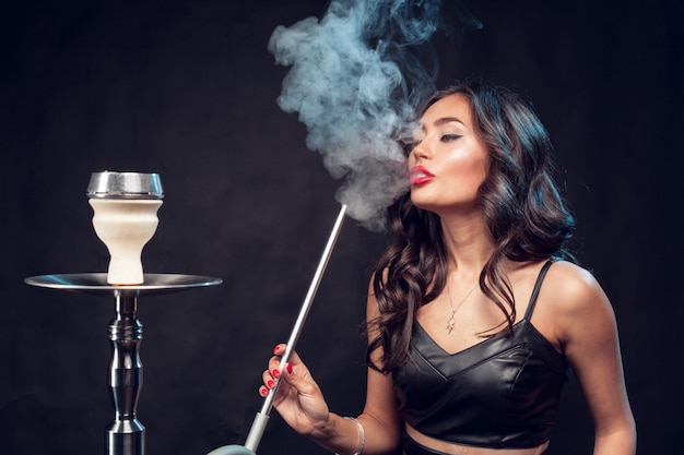 woman smokes hookah / beautiful glamorous woman in black dress smokes a hookah