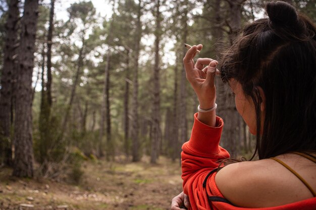 A woman smoking in the woods in a red sweater